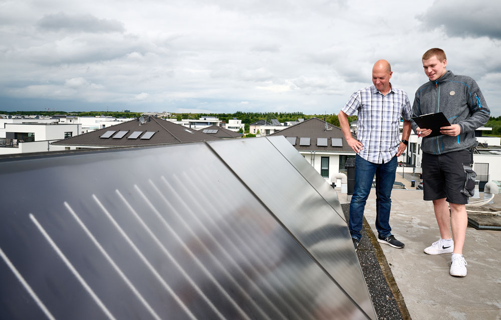 Zwei Männer stehen auf einem Gebäudedach und schauen sich eine installierte Photovoltaikanlage an.