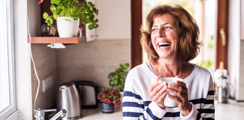Bauherrin in der Küche lacht mit Kaffee-Tasse in der Hand