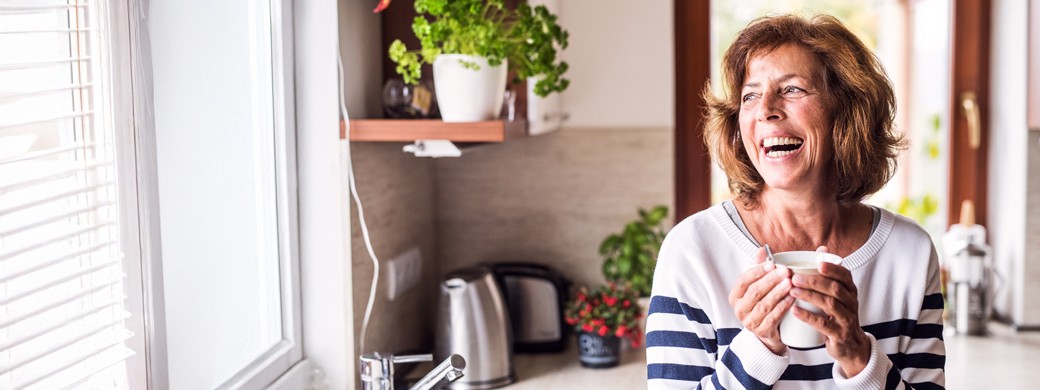 Bauherrin in der Küche lacht mit Kaffee-Tasse in der Hand