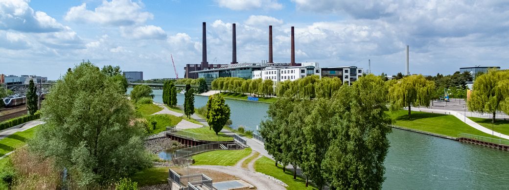 Industriepark mit Fluss, Grünanlagen und Fabrikgebäuden mit Schornsteinen unter bewölktem Himmel