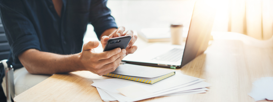 Journalist am Schreibtisch recherchiert via Handy und Laptop zur Öffentlichen Versicherung Braunschweig""