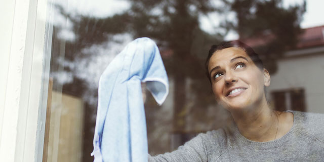 Frau schaut aus dem Fenster und putzt dabei