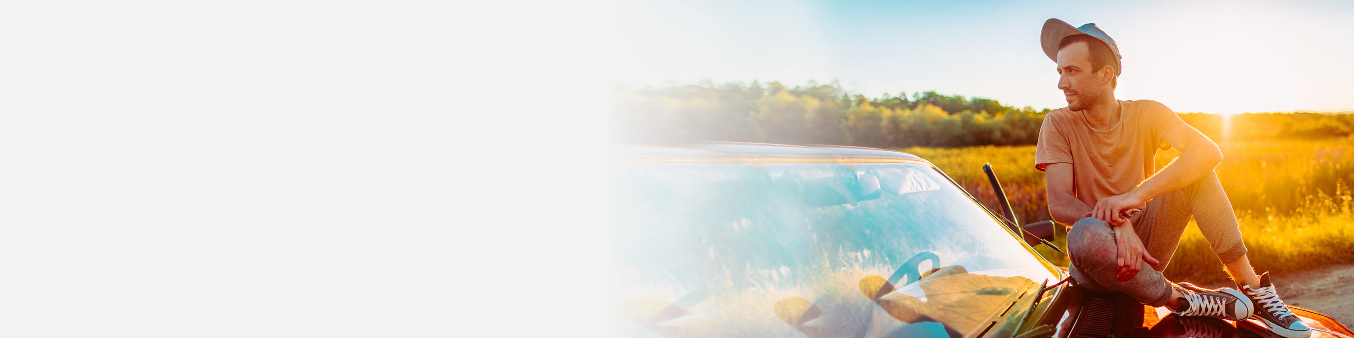 Ein junger Mann sitzt auf seiner Motorhaube im Sonnenuntergang.