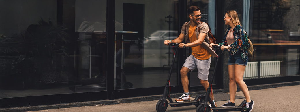 Junges Pärchen mit einer Versicherung für Elektrokleinstfahrzeuge jeweils auf E-Roller unterwegs