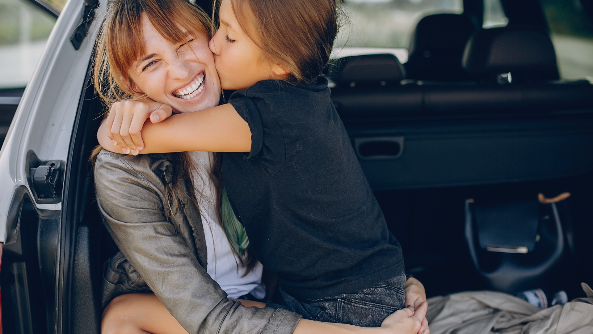 Kundin mit ihrer Tochter im Kofferraum ihres bei der Öffentlichen versicherten Autos sitzend