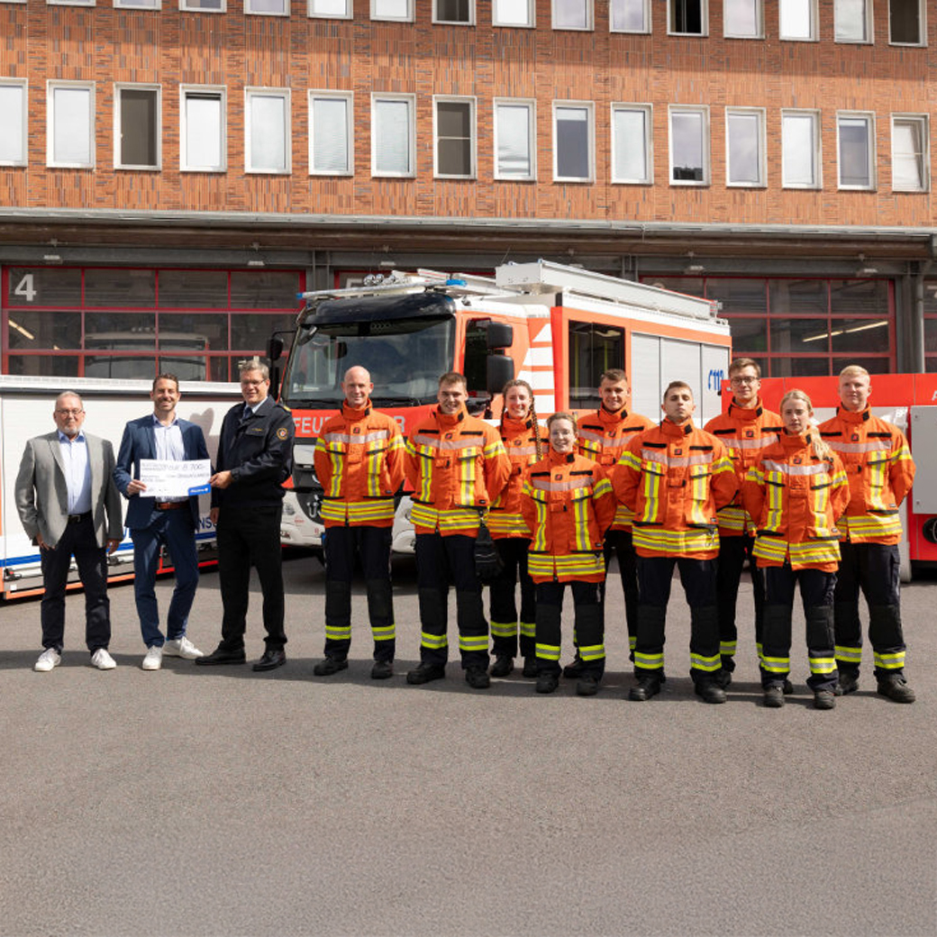 Jens-Folker Huismann und Christoph Mrasek von der Öffentlichen bei der Scheckübergabe an Torge Malchau und die aktuellen Auszubildenden der Braunschweiger Feuerwehr