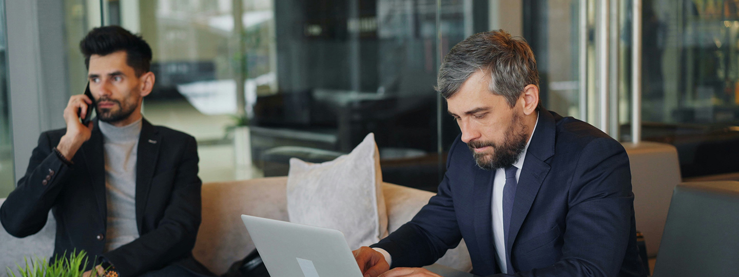 Zwei Kollegen: Einer telefoniert, der andere arbeitet am Laptop