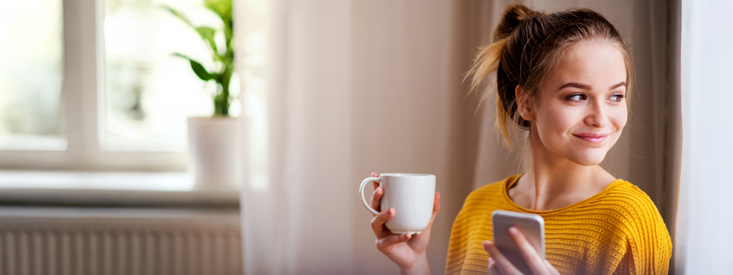 Frau hält Kaffeetasse und Smartphone in der Hand und sucht nach einer Versicherung der Öffentlichen Braunschweig