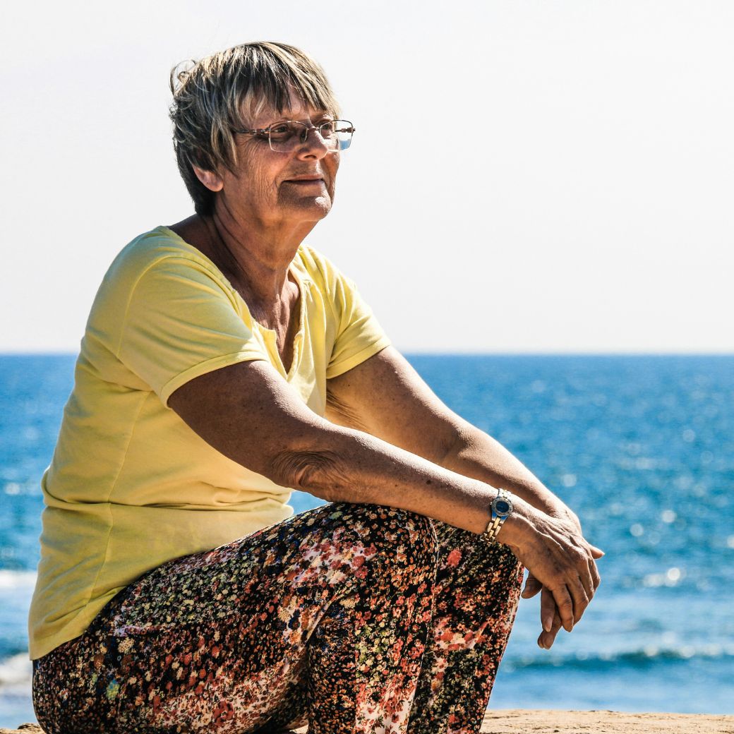 Ältere Frau sitzt am Meer und denkt an ihre Sterbegeldversicherung