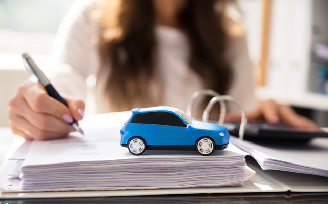 Frau mit Aktenordner und blauem Auto ermittelt Rückkaufwert nach einem Kfz-Schaden