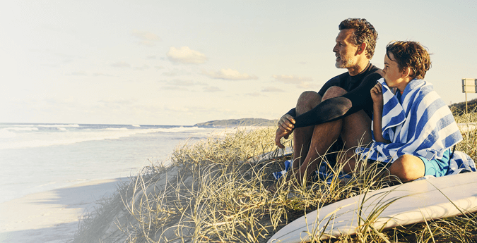 Vater und Sohn sitzen auf einer Düne und blicken auf das Meer