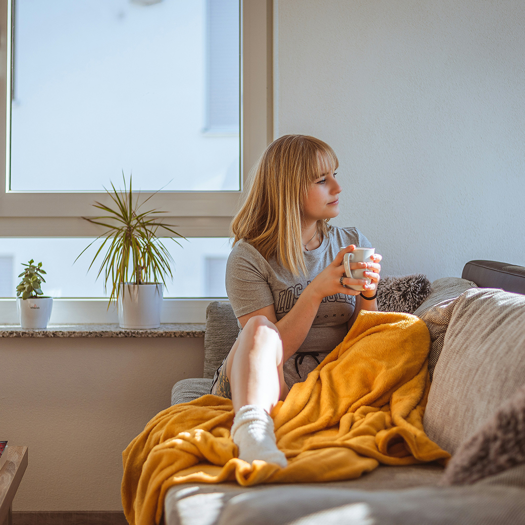 Frau sitzt auf ihrem Sofa im Wohnzimmer