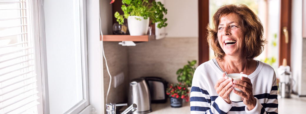 Bauherrin in der Küche lacht mit Kaffee-Tasse in der Hand