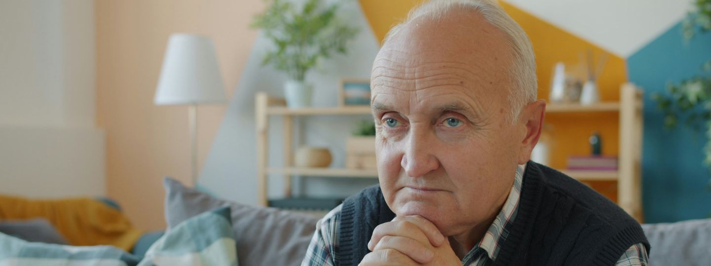 Alter Mann sitzt auf dem Sofa in seinem Wohnzimmer