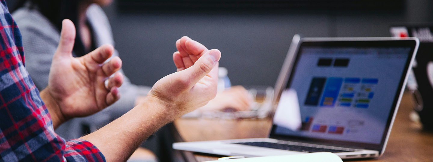Person sitzt vor seinem PC und gestikuliert mit den Händen