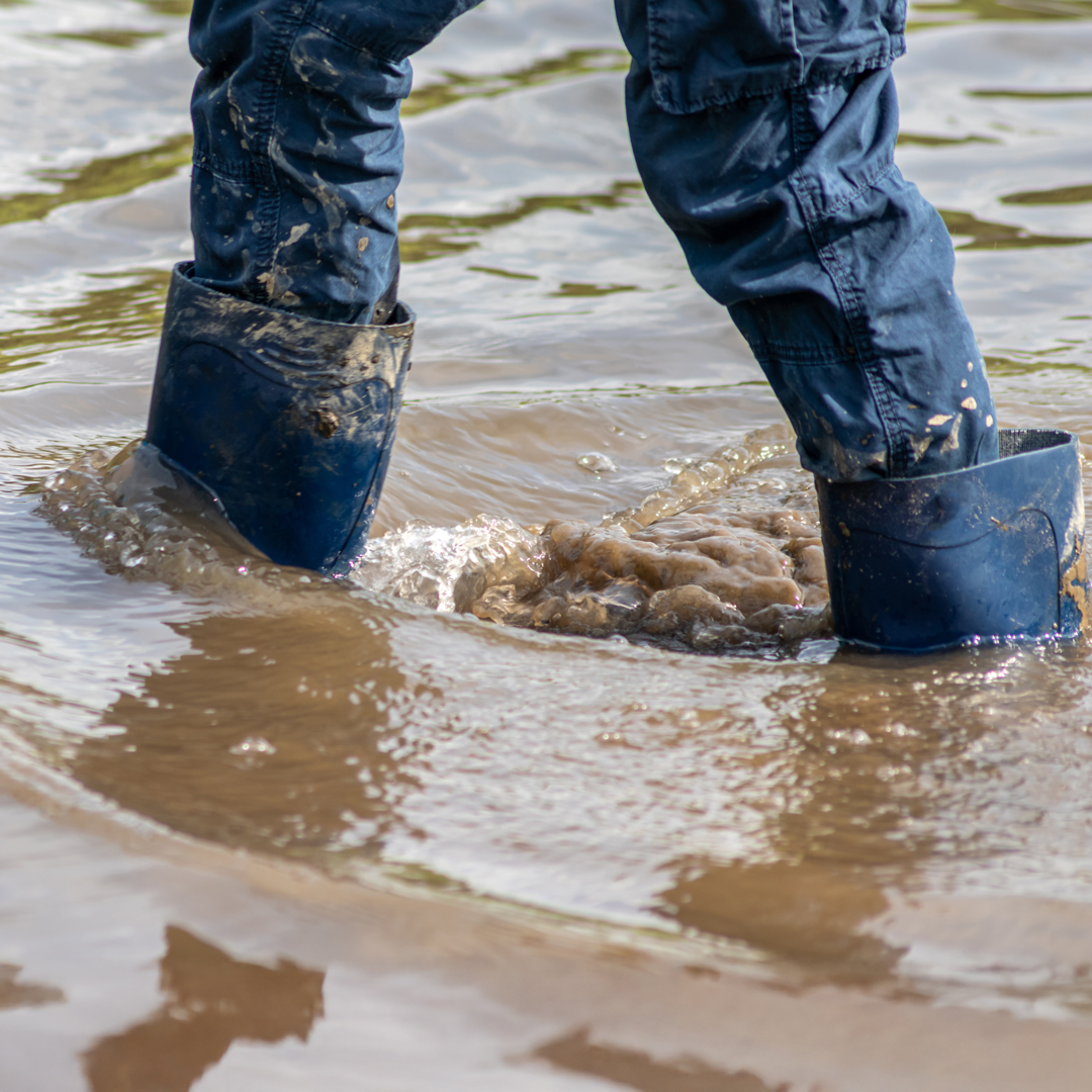Eine Person mit Gummistiefeln die durch das Hochwasser läuft
