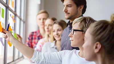 Symboldbild mit Workshop-Teilnehmenden vor Pinnwand mit Klebezetteln für Benefits bei der Öffentlichen Braunschweig: Entwicklungsmöglichkeiten