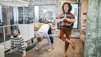 Symboldbild mit drei Personen, die Yoga-Übungen in verglastem Büro machen für Benefits bei der Öffentlichen Braunschweig: Gesund und Aktiv