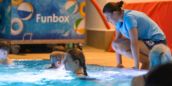 Eine Frau am Beckenrand trainiert Kinder in einem Schwimmbecken