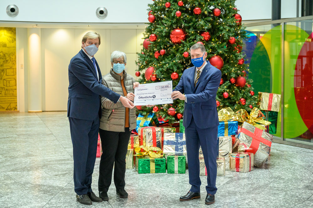 Spendengutschein wird vor einem Weihnachtsbaum übergeben