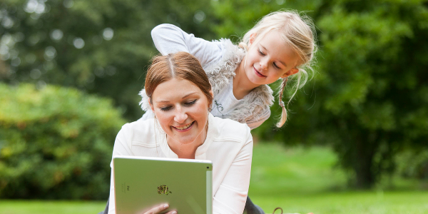 Frau im Park guckt auf Tablet und Kind schaut ihr über die Schulter