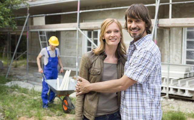 Ein Paar hält sich vor einer Haus-Baustelle im Arm