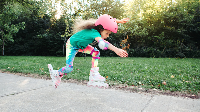 Ein Kind mit Helm und Knie- und Ellenbogenschützern fährt rasant auf Inline-Skates.