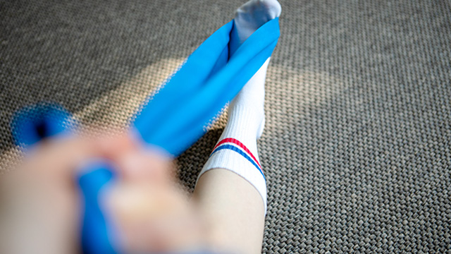 Ein Fuß wird mit einem blauen Theraband mobilisiert.