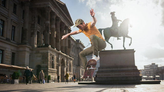 Ein Skater bei einem Sprung auf dem Vorplatz des Braunschweiger Schlosses. Im Hintergrund im Gegenlicht ist eines der beiden Reiterdenkmäler zu sehen.