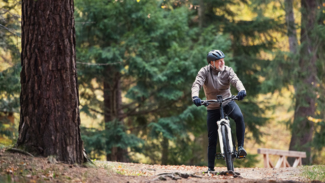 Älterer Mann auf einem Fahrrad im Wald. Der Mann trägt einen Fahrradhelm und sieht sehr agil aus.