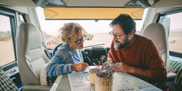 Zwei Menschen sitzen in einem Campingmobil am Tisch und schauen auf eine Karte aus Papier.
