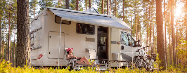 Eine Person ruht sich vor einem Wohnmobil im Wald aus.