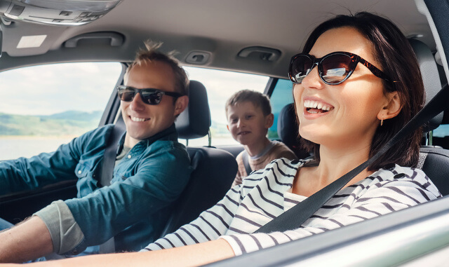 Familie lachend im Auto bei offenem Fenster