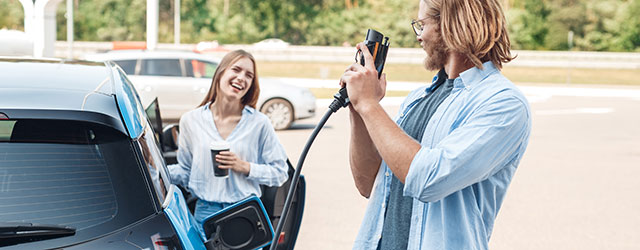 Zwei Personen stehen an einem Auto. Eine Person hat einen Stecker für
