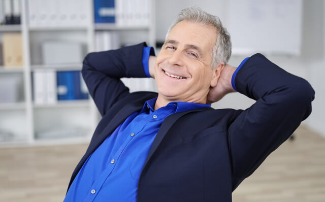 Ein Mann mittleren Alters lehnt sich in entspannter Pose zurück, er trägt ein dunkelblaues Hemd und ein legeres Jackett. Bestimmt ist er froh clever mit der LöwenRente vorgesorgt zu haben