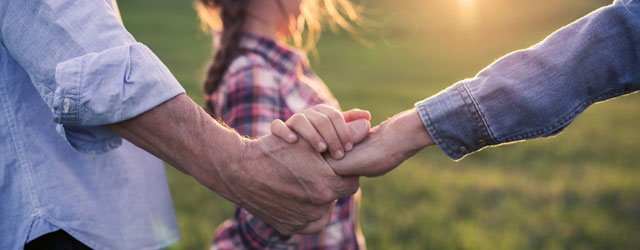 Großeltern mit Enkelin halten sich an den Händen in sommerlicher Abendstimmung