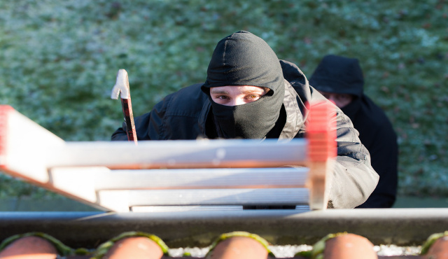 Einbrecher klettert über eine Leiter auf das Dach