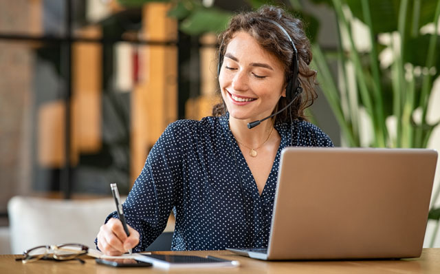 Eine Frau sitz mit Headset am Laptop